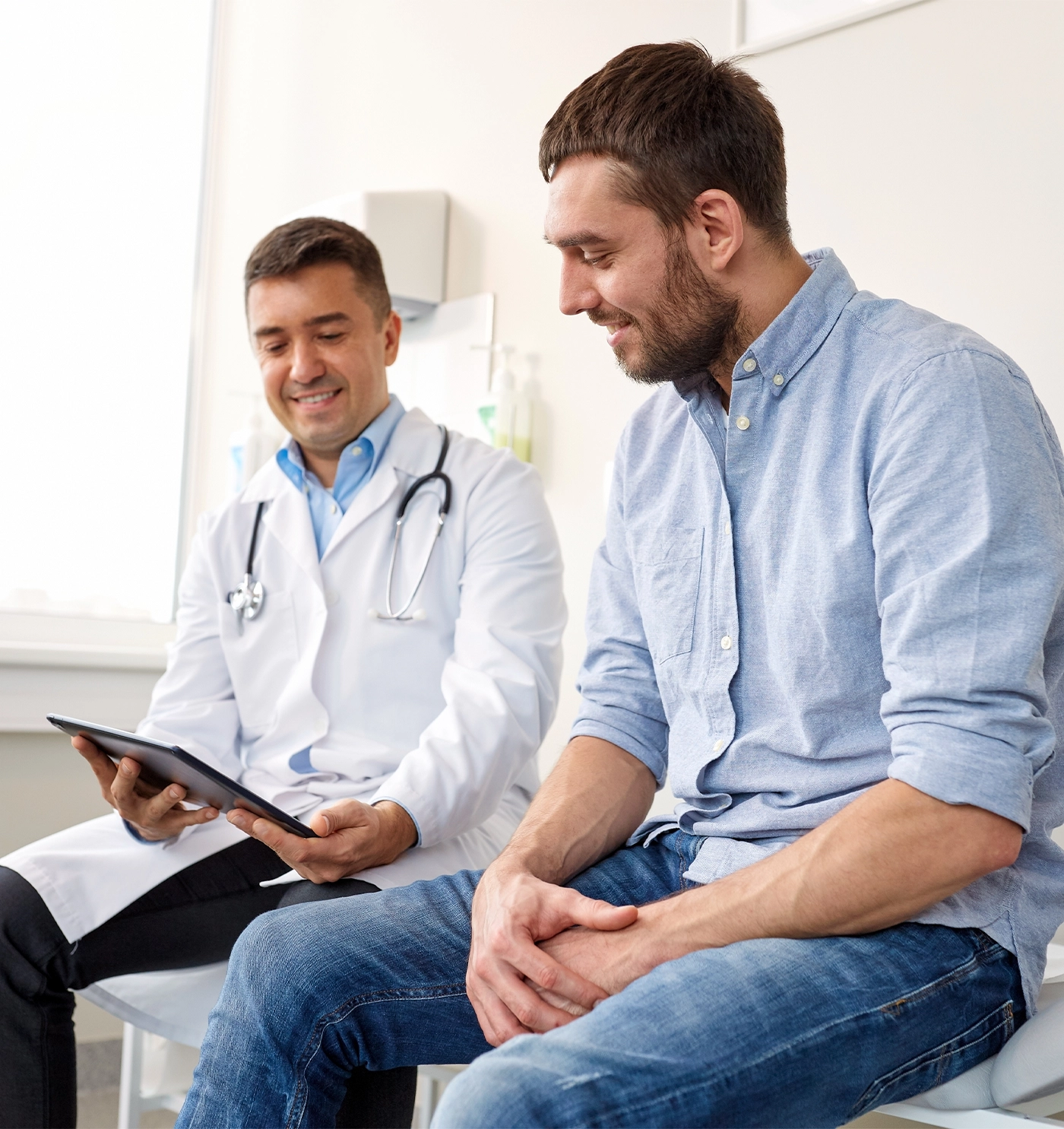 smiling doctor with tablet pc computer and young man patient meeting